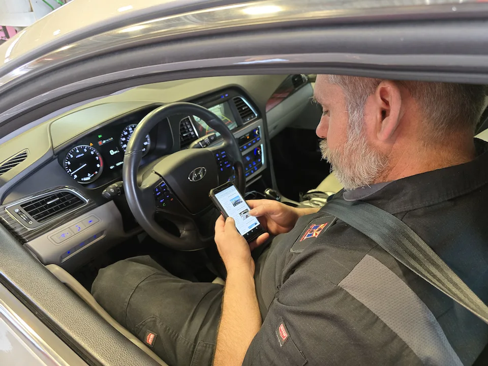 man on smart phone trying to troubleshoot car at mechanic shop